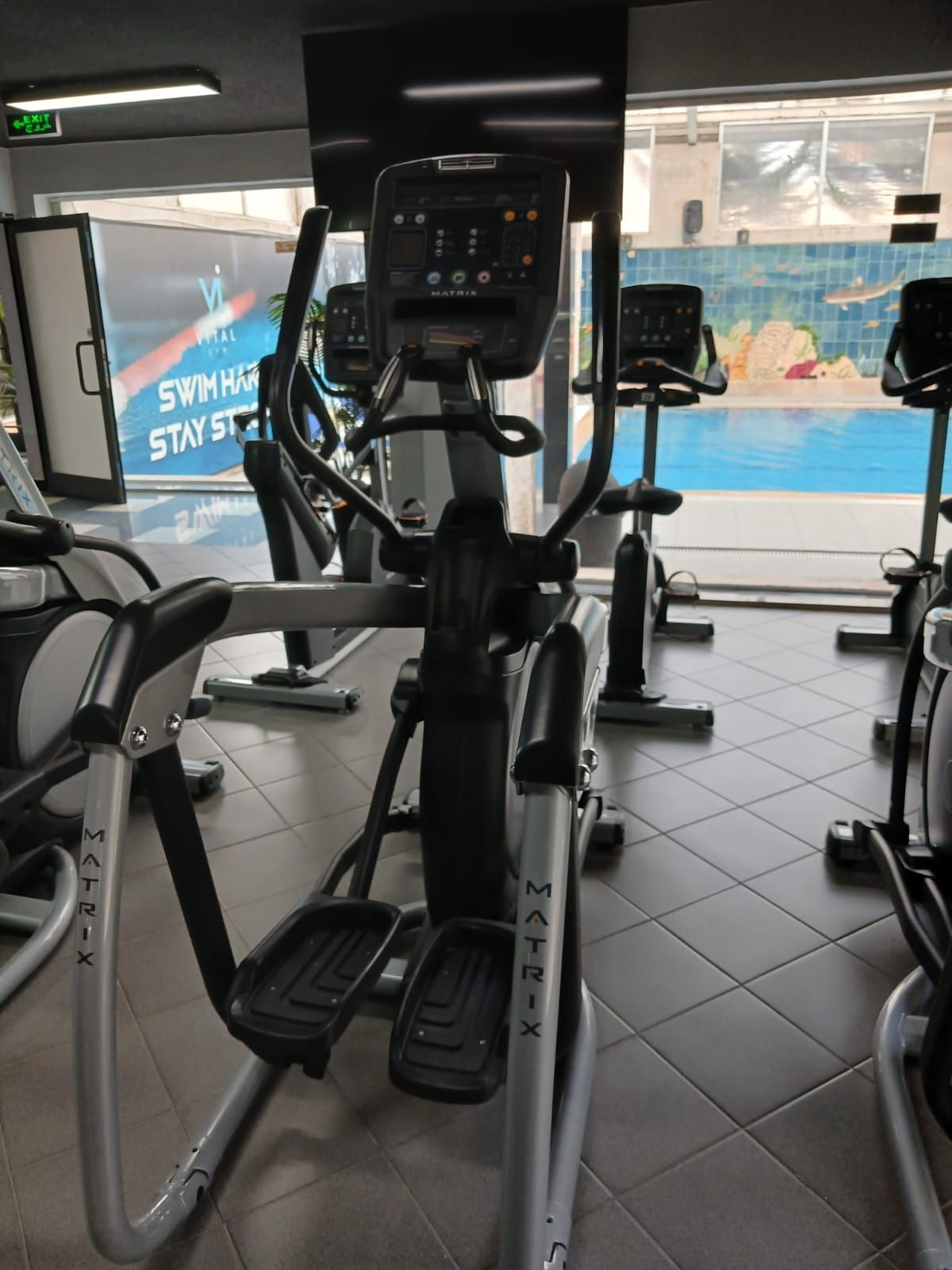 Een fitnessruimte met hometrainers, een loopband en uitzicht op het zwembad.