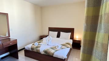 Ein Hotelzimmer mit Bett, Nachttischen, einem Spiegel und einem Vorhang.