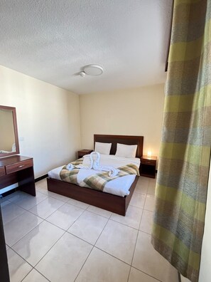 Una habitación de hotel con una cama, mesitas de noche, un espejo y una cortina.
