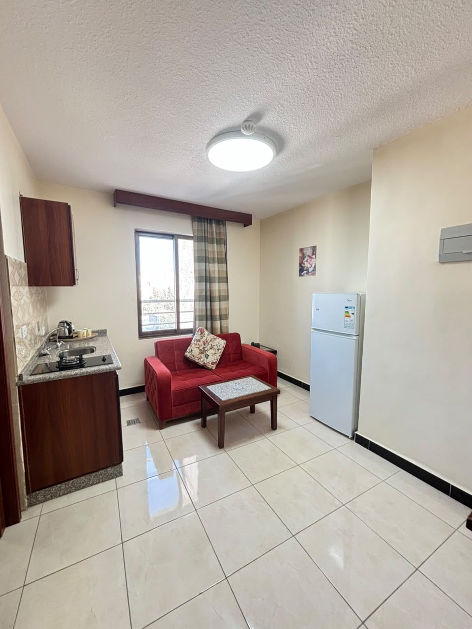 A compact living space with a kitchenette, a red sofa, a small table, and a refrigerator.