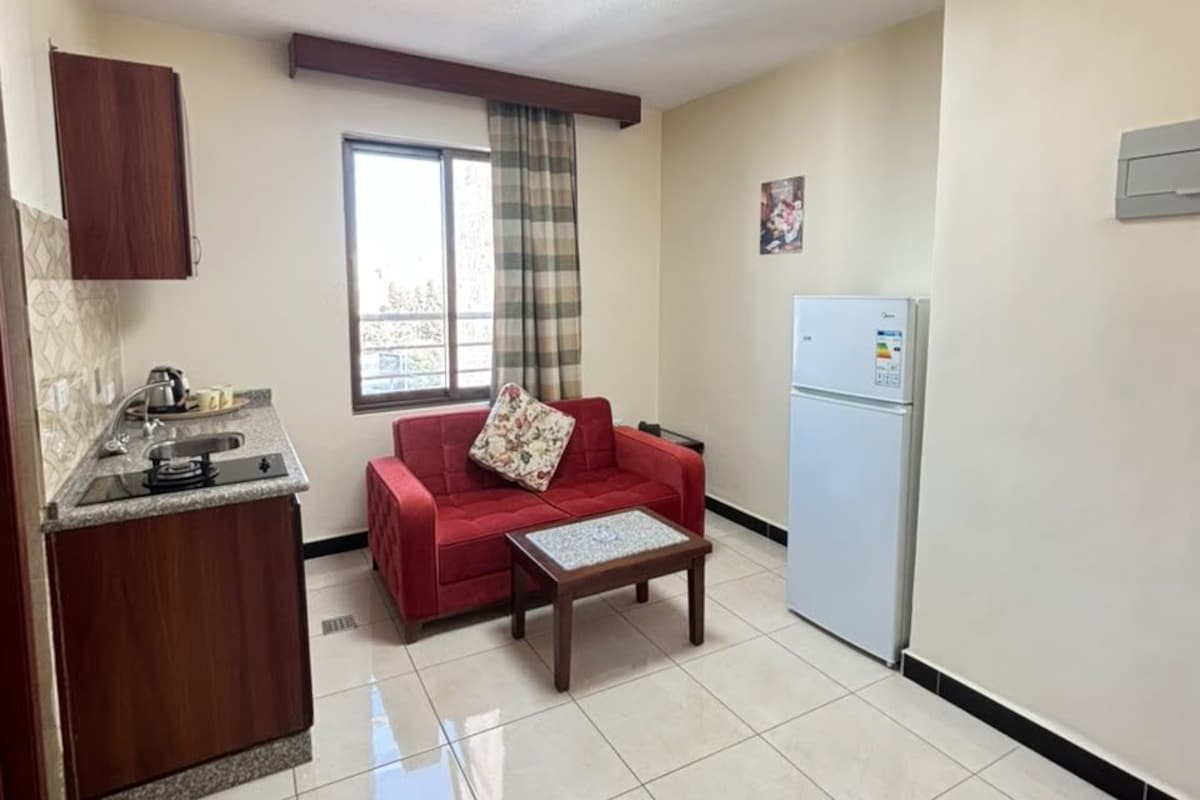 A compact living space with a kitchenette, a red sofa, a small table, and a refrigerator.