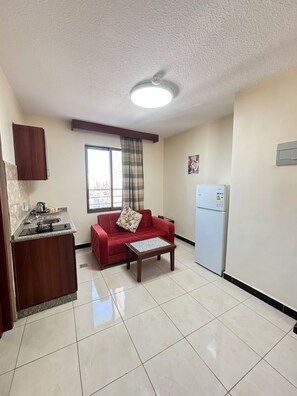 Un espacio habitable compacto con kitchenette, un sofá rojo, una mesita y un refrigerador.