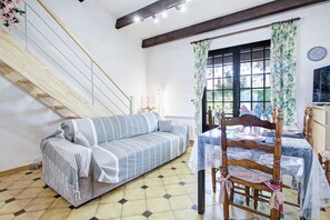 A room with a sofa, a dining table, a chair, a staircase, and a window with curtains. - L'Écrin de Saint-Cyprien - 2km du Port (Saint-Cyprien)