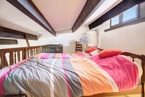 Ein Schlafzimmer mit einem hölzernen Bett, bunter Bettwäsche, einer kleinen Kommode und einem Fenster.