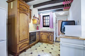 A kitchen with wooden cabinets, a tiled floor, a red coffee maker, and a white refrigerator. - L'Écrin de Saint-Cyprien - 2km du Port (Saint-Cyprien)
