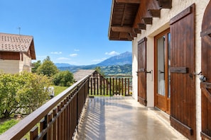 A balcony with a view of mountains, a wooden fence, and a building with large wooden doors. - Chalet Edelweiss - Station ski accessible à pied (Saint-Léger-les-Mélèzes)