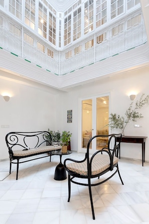 A spacious indoor area with a high ceiling, a seating arrangement, and a view through a glass door. - Genteel Home Patio del Arenal 001 (Seville)