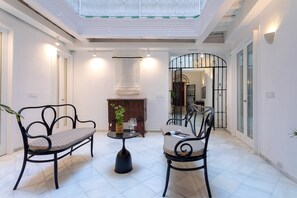 Un hall d’entrée spacieux, avec deux chaises en métal noir, une petite table ronde et une plante en pot.