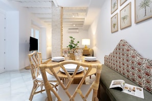 A dining area with a table set for two, a sofa with a floral cushion, and a magazine on the sofa. - Genteel Home Patio del Arenal 001 (Seville)
