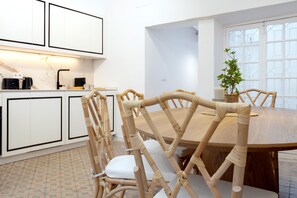Eine moderne Küche mit weißen Schränken, einer schwarzen Kaffeemaschine und einem Essbereich mit einem Holztisch und Stühlen.