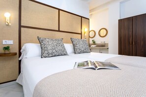 A hotel room with a bed, two pillows, a bedside table with a plant, a wall-mounted light, a mirror, and a wardrobe. - Genteel Home Patio del Arenal 201 (Seville)