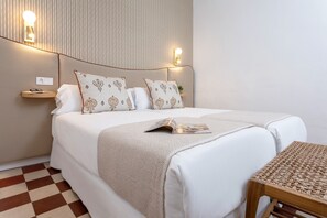Een netjes opgemaakt bed met gestreepte kussens, een nachtkastje met een lamp en een tijdschrift op het bed.