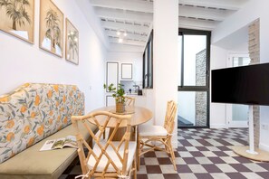 Een moderne woonkamer met een zwart-wit geruite vloer, een bank met bloemenprint, een eettafel met stoelen en een flatscreen televisie.