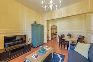 A living room with a television, a cabinet, a dining table with chairs, and a sofa. - Sunflower Suite by MMega (Firenze)