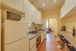 A compact kitchen with a built-in microwave, gas stove, and oven. There is a bar area with stools and a coffee machine. - Sunflower Suite by MMega (Firenze)