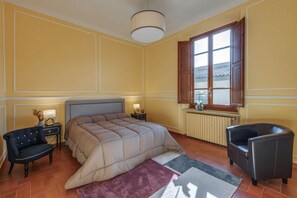 A bedroom with a bed, two nightstands, a chair, a window, and a radiator. - Sunflower Suite by MMega (Firenze)