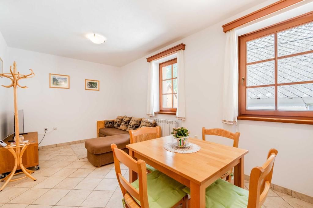 Una stanza con un tavolo da pranzo in legno, un divano marrone, un appendiabiti in legno e una finestra con vista su un edificio.