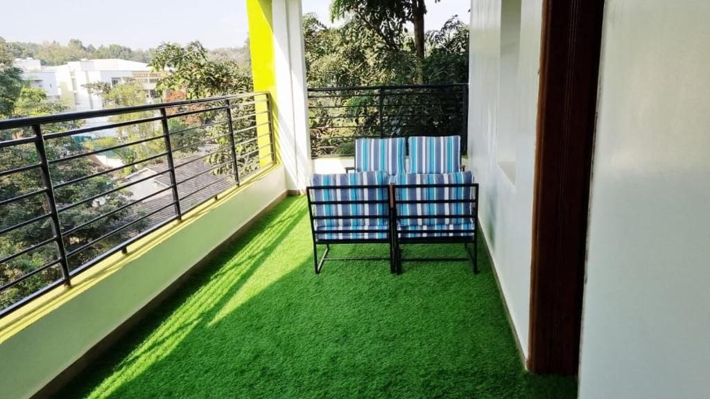 A balcony with artificial grass, a metal railing, and a blue-striped chair.