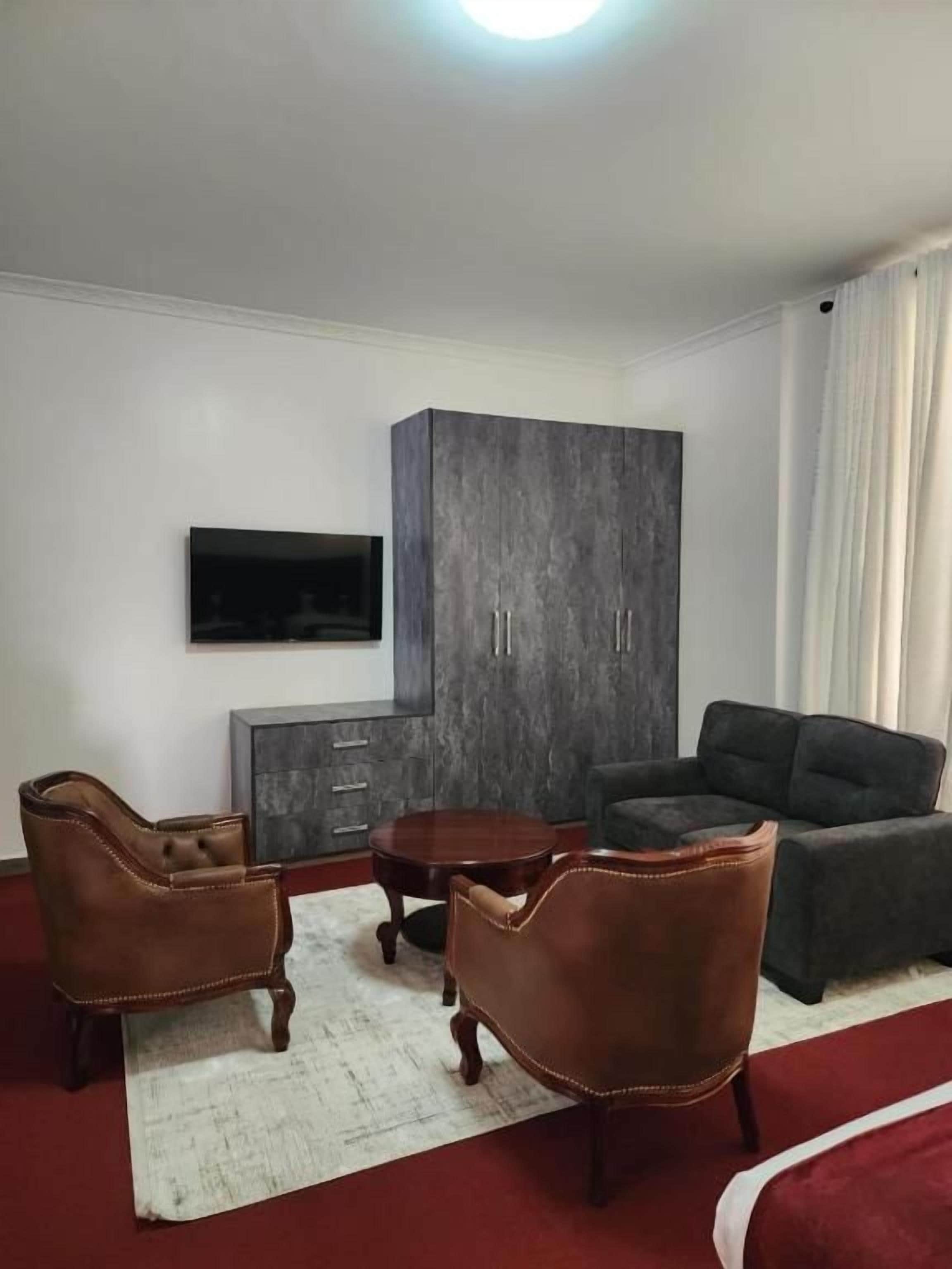 A living room with a flat-screen TV, dark-colored furniture, and a red carpet.