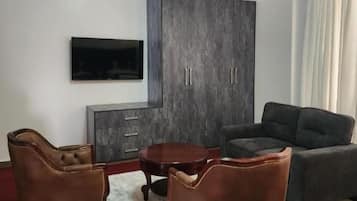 A living room with a flat-screen TV, dark-colored furniture, and a red carpet.