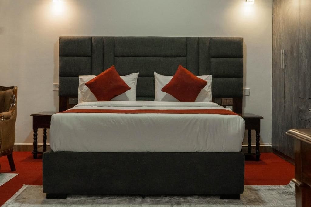Una cama con cabecera oscura, ropa de cama blanca y almohadas rojas. Hay dos mesitas de noche con lámparas.