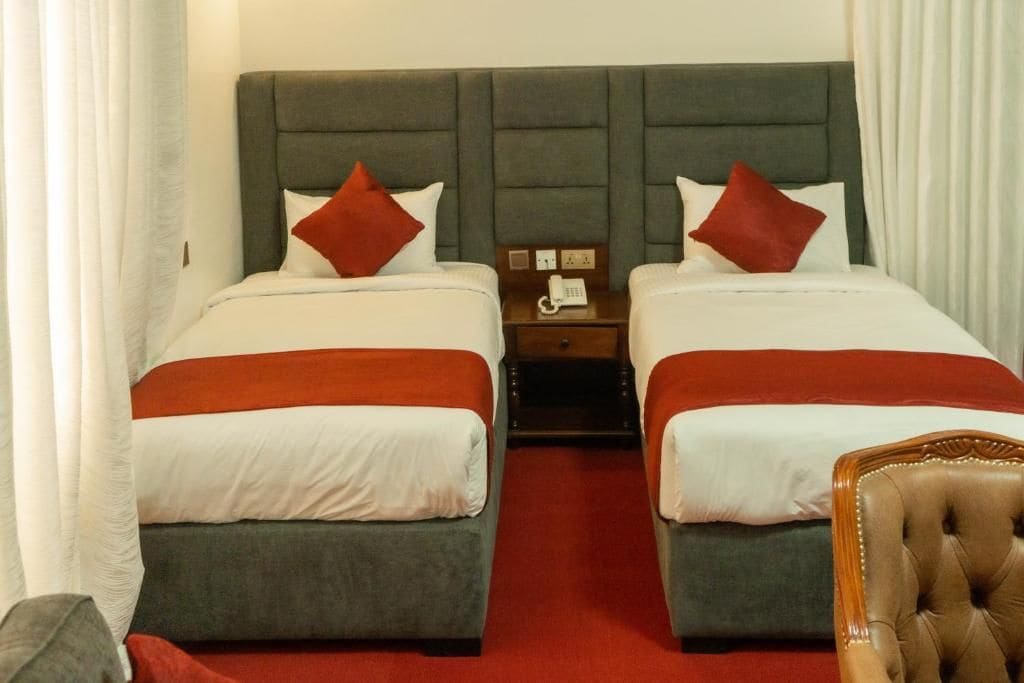 A hotel room with two beds, each with a red pillow, a wooden nightstand with a phone, and a red carpet.