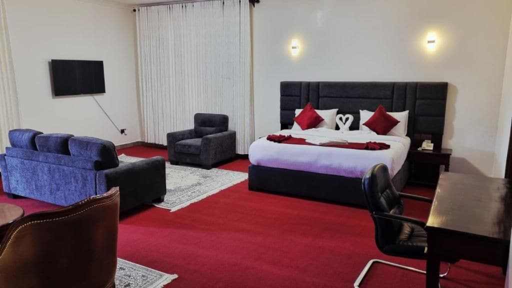 A hotel room with a large bed, a flat-screen TV, a sofa, a chair, and a small table.
