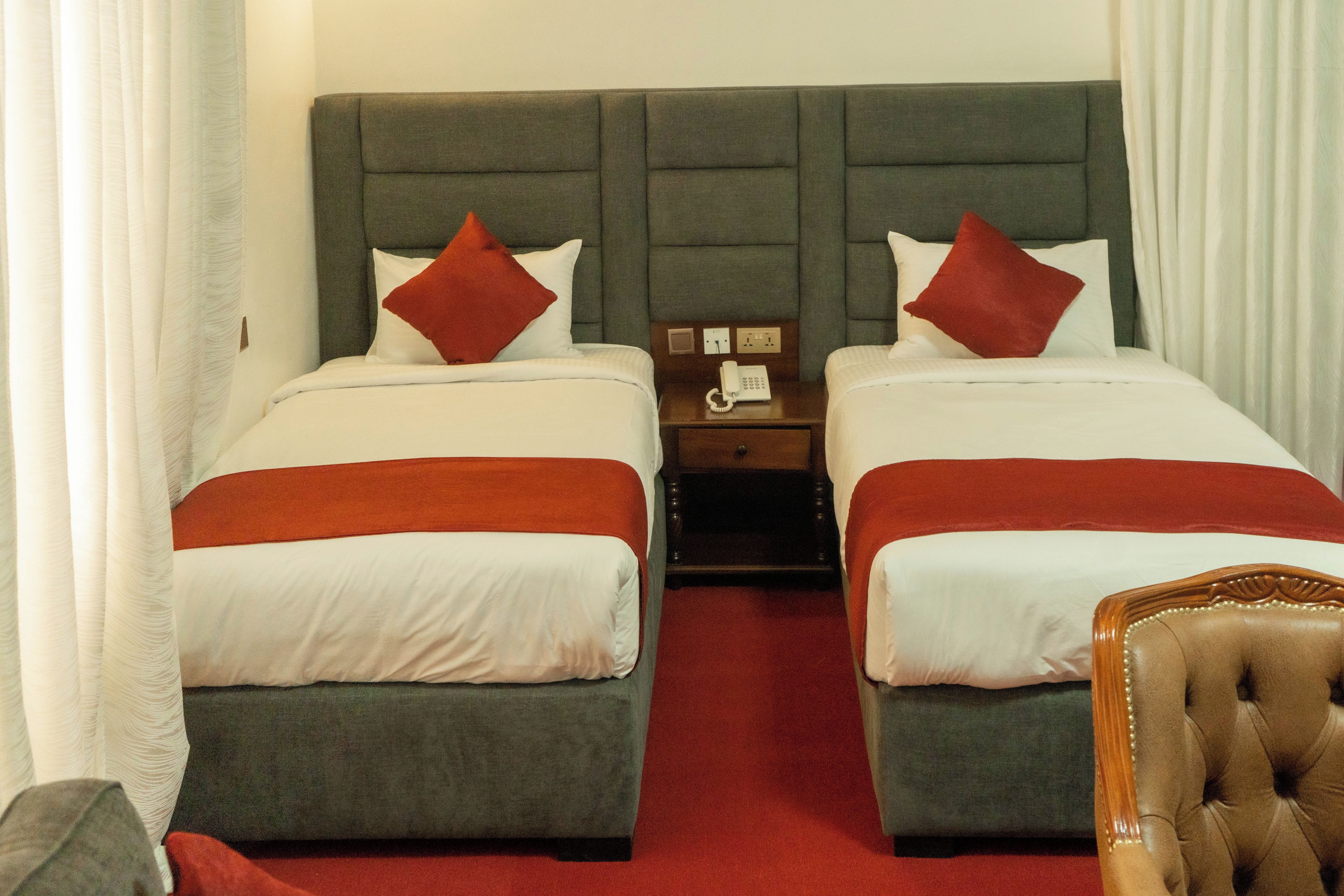 Une chambre d’hôtel avec deux lits, une moquette rouge et une table de chevet en bois avec un téléphone.