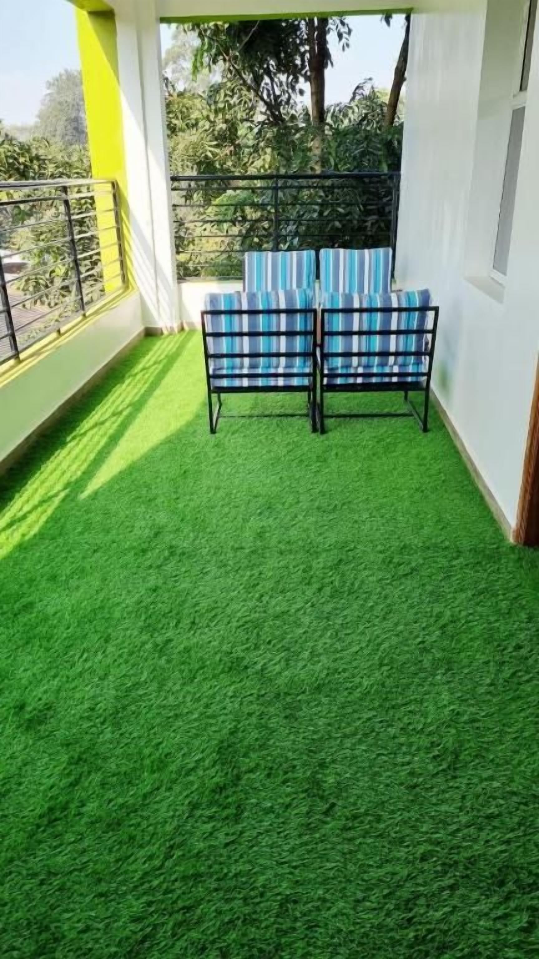 A balcony with artificial green turf, two plaid-patterned chairs, and a railing.