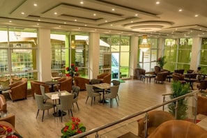 A spacious indoor area with multiple seating arrangements, including tables and chairs, and large windows allowing natural light. - GRANADA HOTEL NAIROBI  (Westlands)