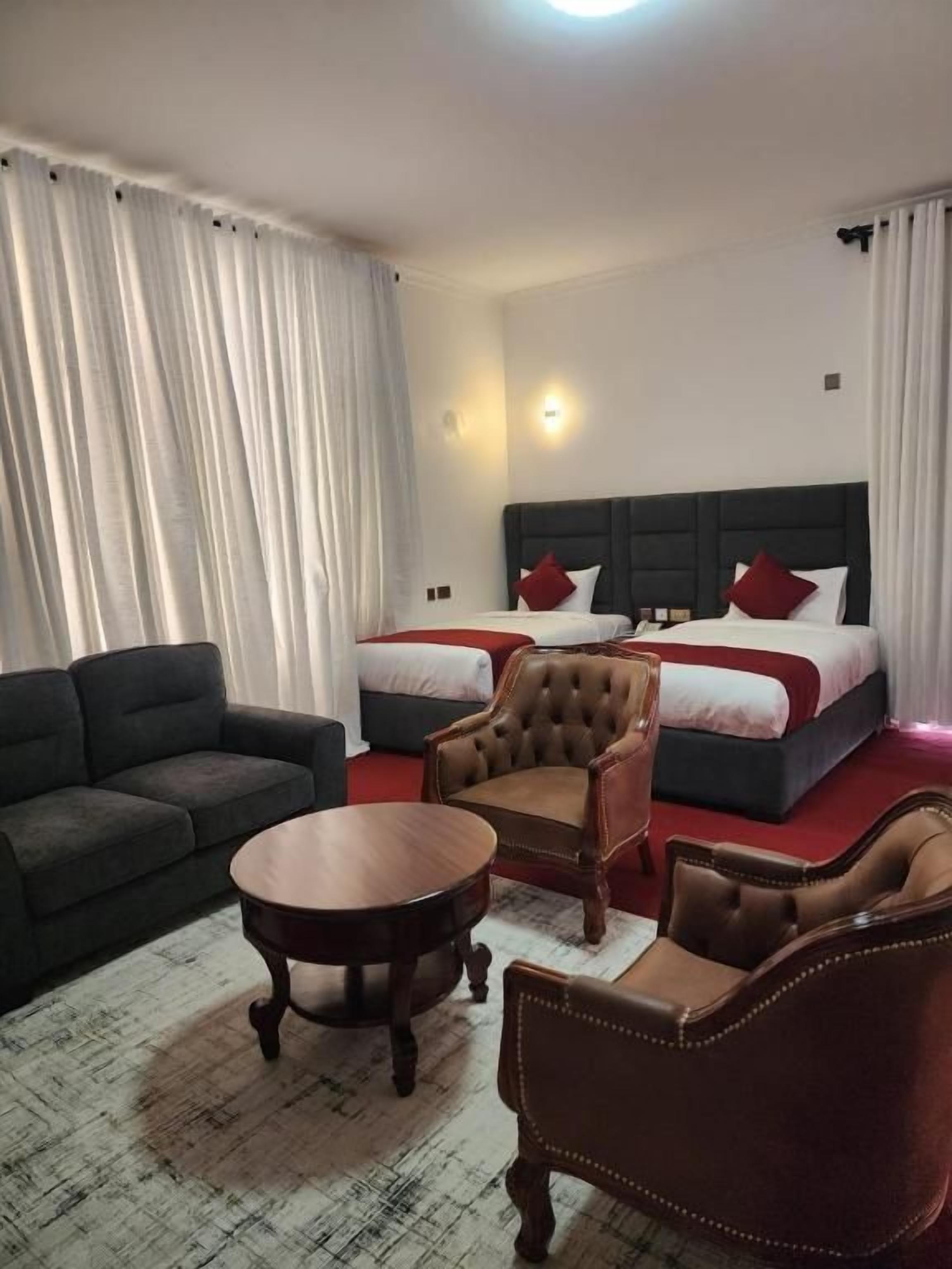 A hotel room with two beds, a sofa, a chair, and a small table.