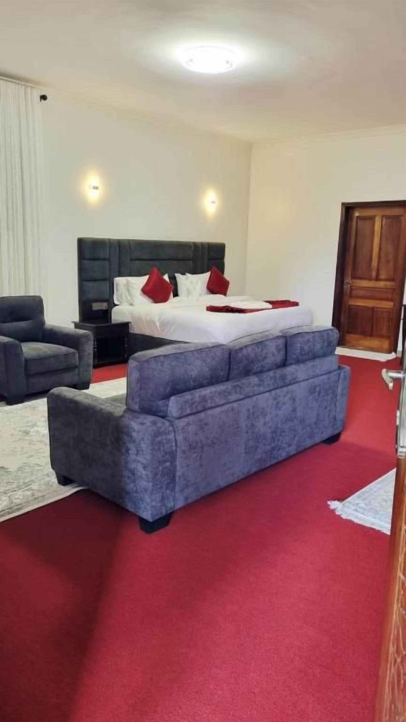 Habitación de hotel con cama, sofá, sillón y piso alfombrado.
