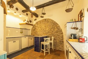 Una cocina con arco de piedra, armarios blancos y utensilios colgantes.