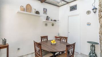 A dining area with a round table, four chairs, and a bowl of lemons. There are two shelves above the table with various items.