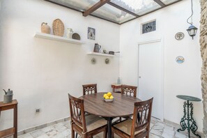Un comedor con una mesa redonda, cuatro sillas y un cuenco de limones. Hay dos estantes sobre la mesa con diversos objetos.