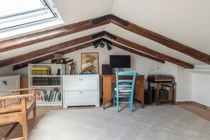 A room with a sloped ceiling, wooden beams, a desk with a chair, a bookshelf, and a flat-screen TV. - Borgo 1660 - Dimora di Charme (Castellabate)
