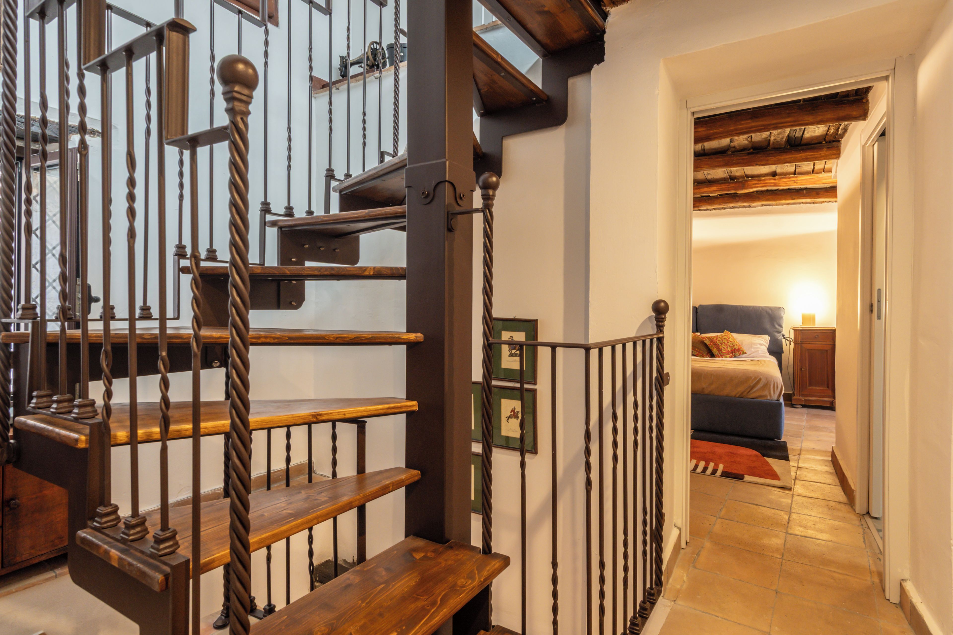 A staircase with wooden steps and metal railings, leading to a bedroom with a bed and a nightstand.