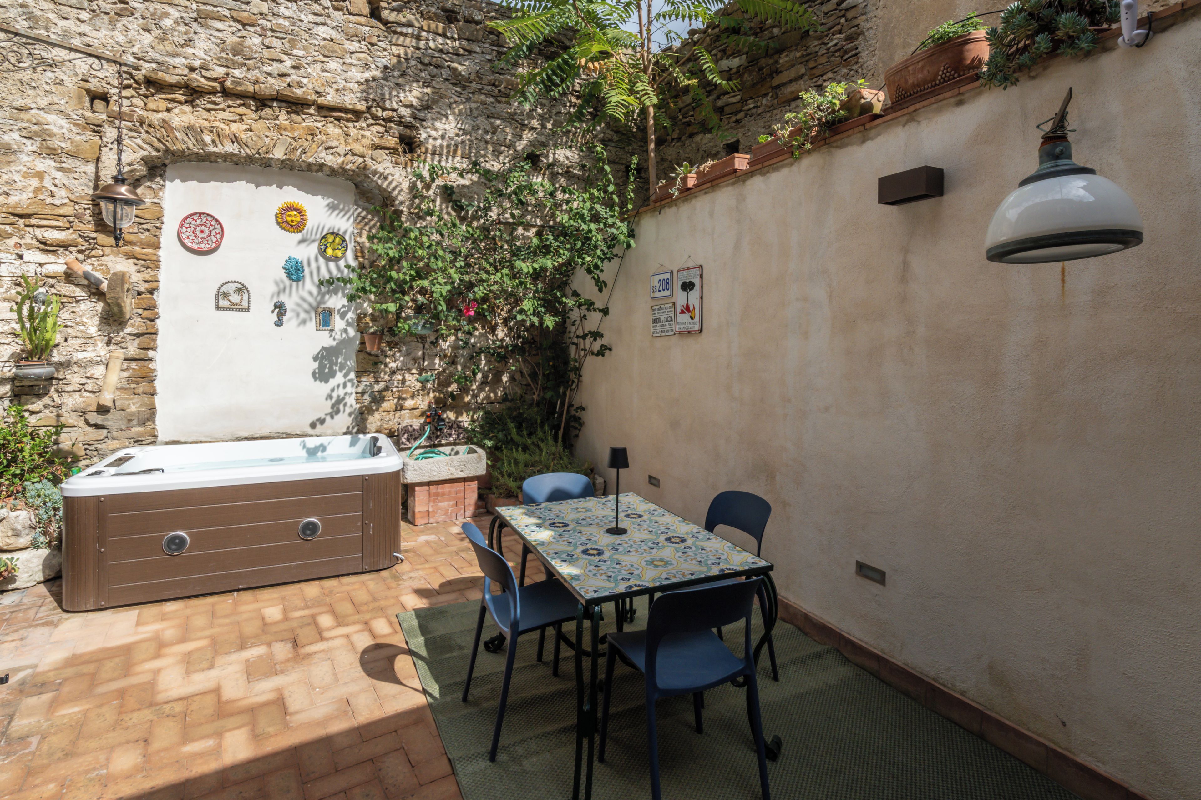 A patio with a hot tub, table, chairs, and a stone wall with plants.
