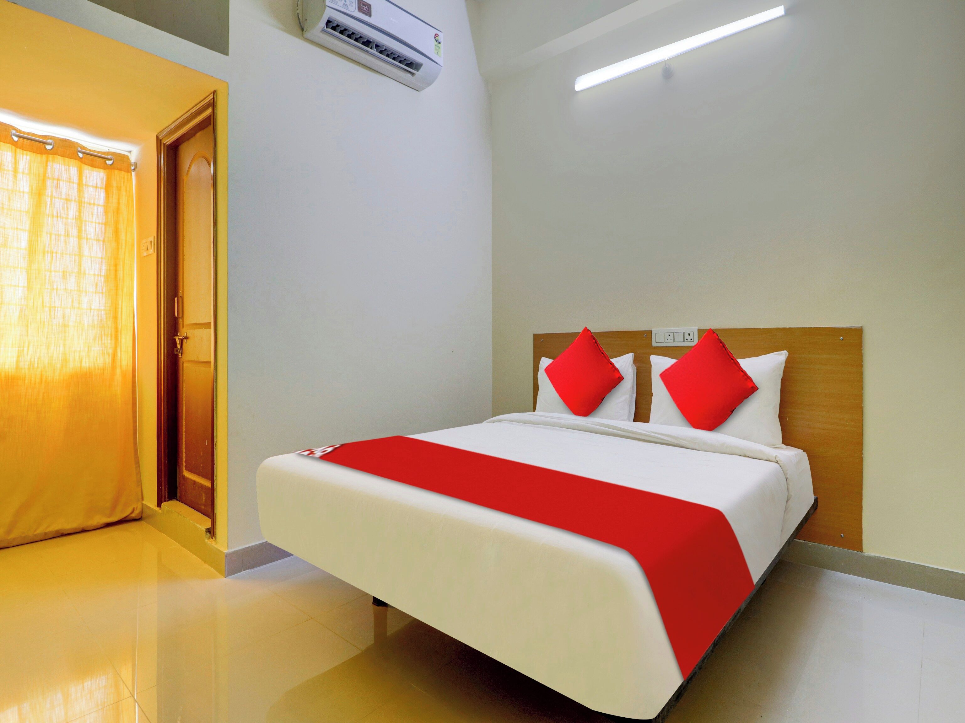 Une chambre d’hôtel avec un lit, une tête de lit en bois, une couvre-lit rouge et blanche et un appareil de climatisation fixé au plafond.