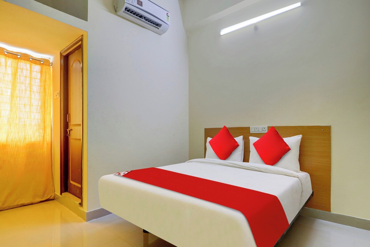 Habitación de hotel con una cama, cabecera de madera, colcha roja y blanca y un equipo de aire acondicionado instalado en el techo.