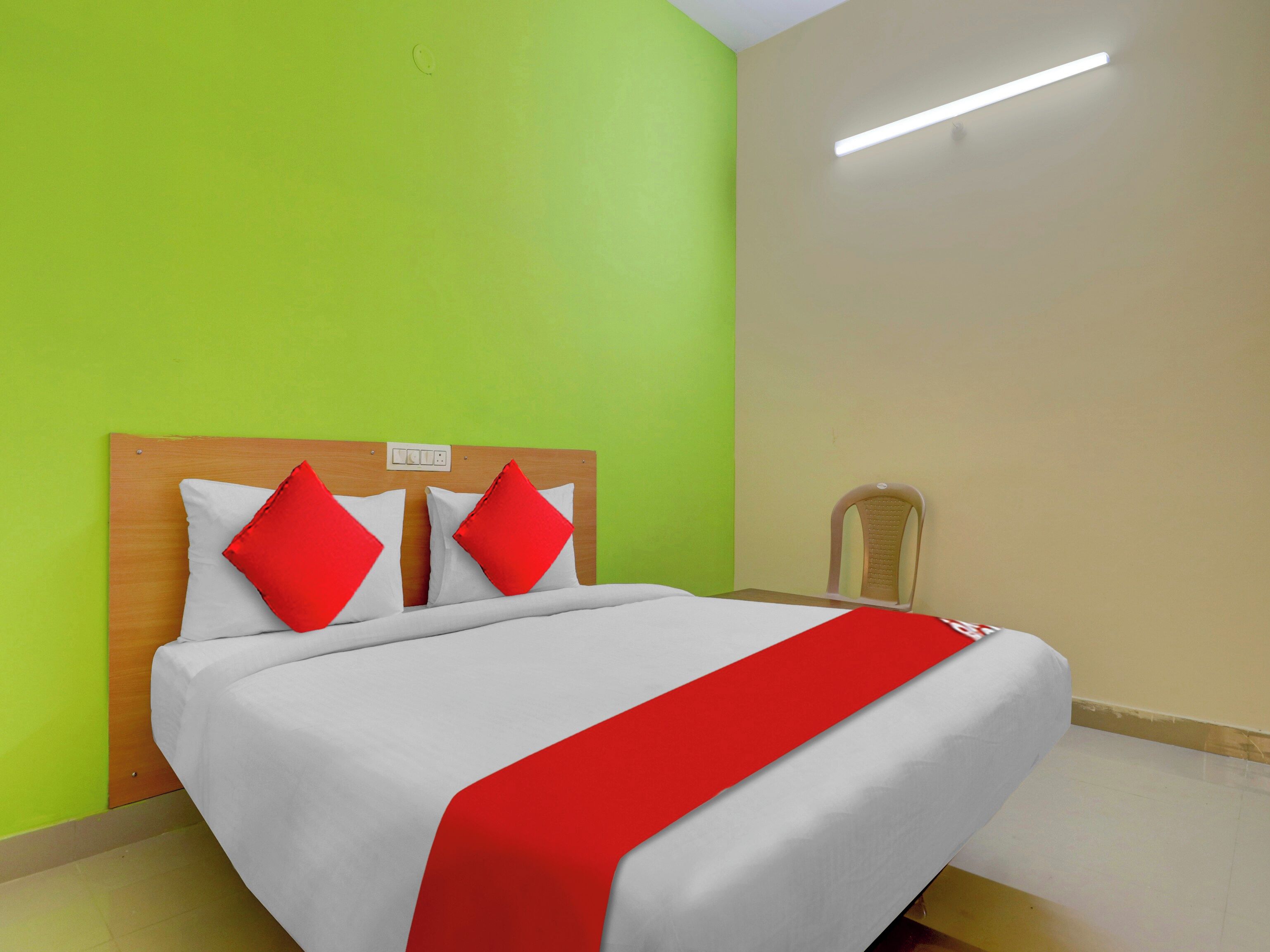 Una habitación de hotel con una cama, una mesita de noche, una silla y una lámpara fijada a la pared.