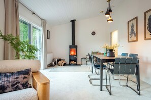 A cozy living room with a fireplace, a dining area with chairs, and a large window providing natural light. - Secluded house on 12 acres, set in the tree canopy, loch views and private beach (Strathtumel)