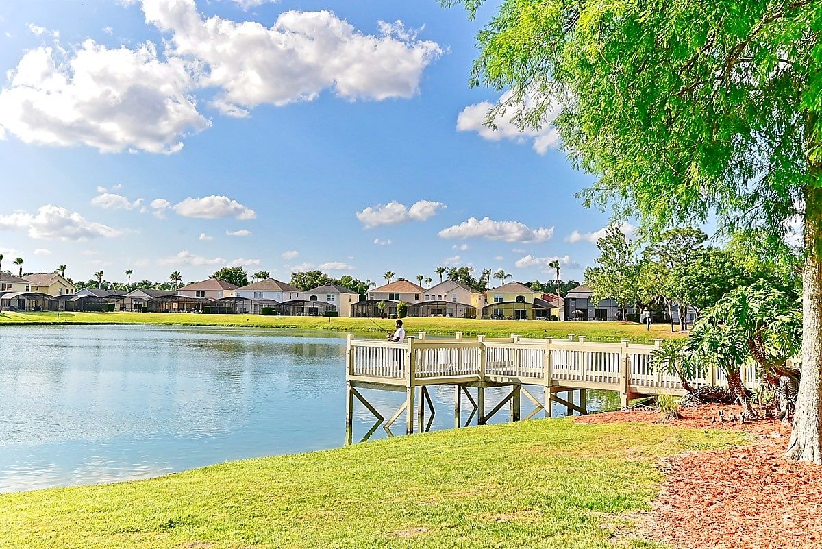 A residential area with a lake, a wooden dock, and houses in the background.