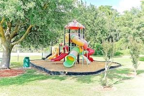 A playground with multiple slides and a climbing structure, surrounded by trees and grass. - Roomy 3-Bed/2.5-Bath Townhome - Disney (Kissimmee)