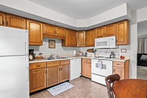 A compact kitchen with wooden cabinets, a white refrigerator, a microwave, a stove, and a dishwasher. - Lynnhaven Landing – Cozy Springfield Getaway (Springfield)