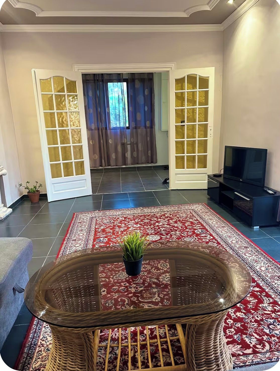 A living room with a glass-top coffee table, a television, and a red patterned rug.