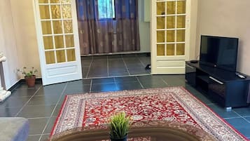 A living room with a glass-top coffee table, a television, and a red patterned rug.