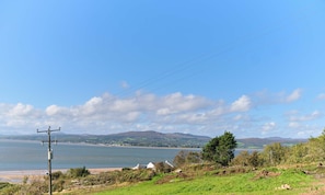 Eine Küstenlandschaft mit blauem Himmel, einem Gewässer und sanften Hügeln in der Ferne.