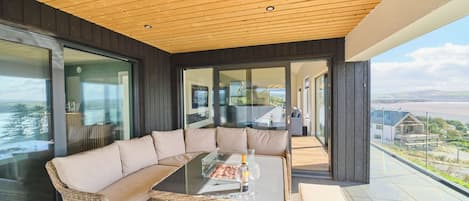 A modern outdoor seating area with a glass-top table, wicker furniture, and a view of the landscape.