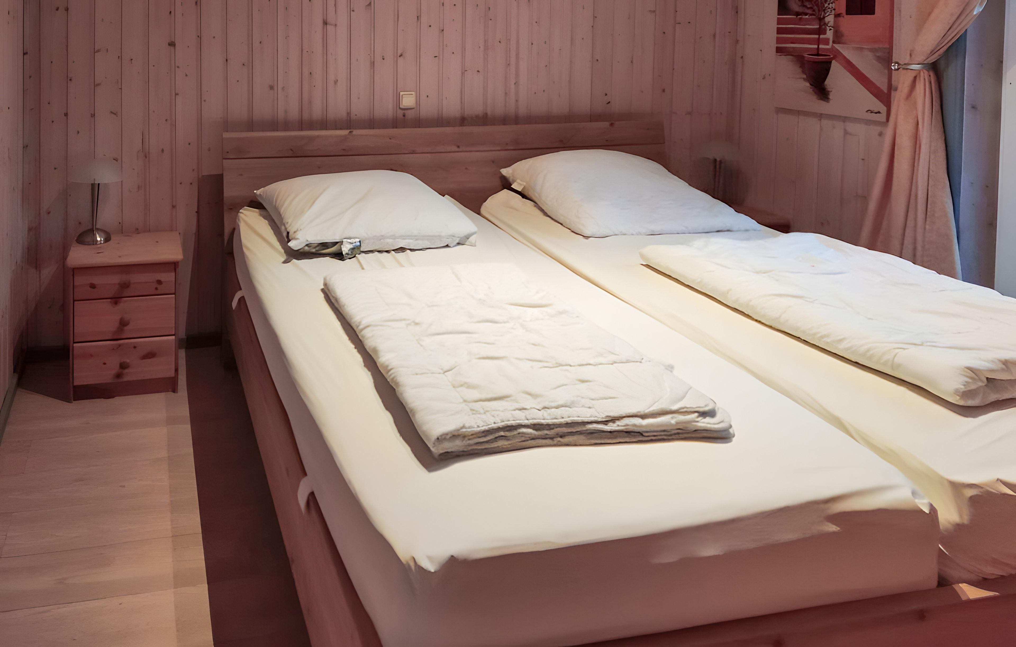 Cama doble con ropa de cama blanca en una habitación con paredes de madera y una mesita de noche.